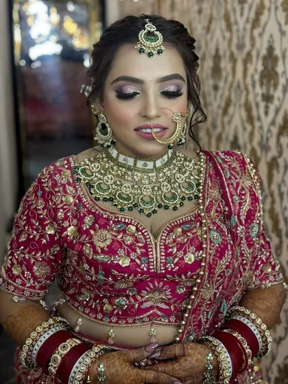 A close-up of a bride in a magenta lehenga. The makeup features a soft cut-crease with pink glitter, paired with a matching lip color for a cohesive and beautiful look.