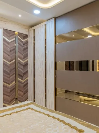This bedroom in Mahad showcases a custom wardrobe with mirrored and textured panels. The adjacent wall features a chevron wood pattern with brass inlays, demonstrating our attention to detailed craftsmanship.