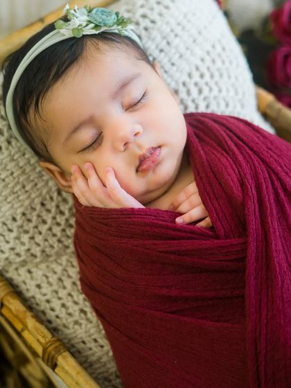 A sweet newborn girl wrapped in a deep red cloth. Her peaceful expression and tiny hands create a portrait of pure innocence.