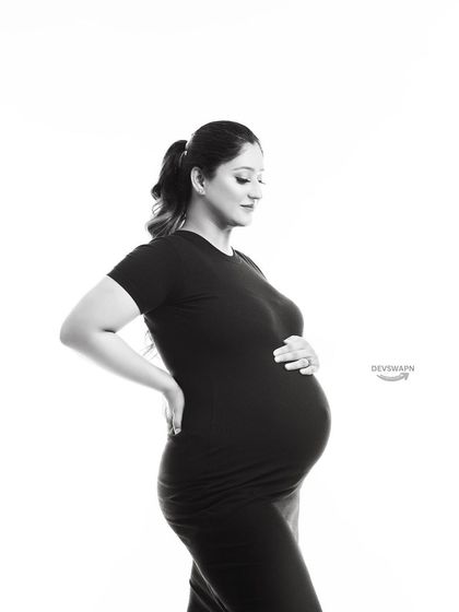 A classic black and white maternity portrait. The simple black dress and clean white background create a timeless, high-contrast image that beautifully highlights the client's form.