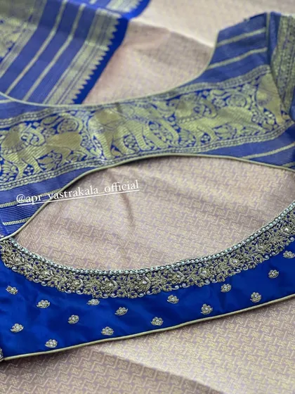 A classic deep U-back design on a royal blue blouse. The top panel features a woven elephant motif, while the lower edge is finished with silver embroidery.