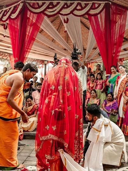 A wide shot of a South Indian wedding ceremony taking place in a beautiful outdoor mandap, with family and guests looking on.