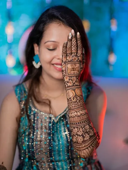 A classic mehendi pose, with the bride showcasing the intricate design on her hand. The detailed henna art is the star of this shot.