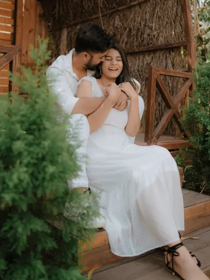 A moment of pure, uninhibited laughter on a rustic wooden porch. Dressed in coordinated white, this couple's joy is infectious, showcasing a perfectly candid moment from their pre-wedding shoot.