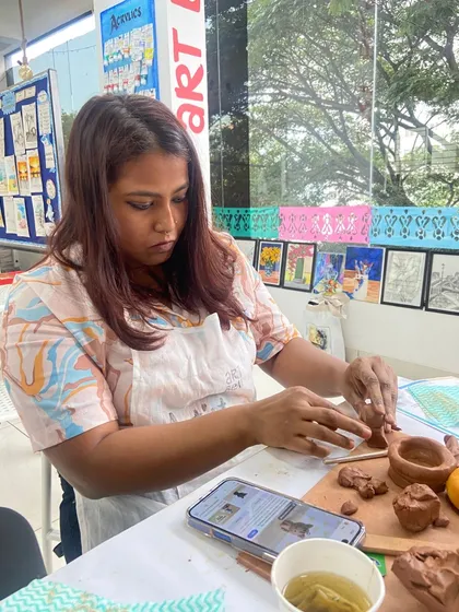 A participant works on her clay piece, using a smartphone for reference. You can bring your own ideas or get inspired by the projects we offer.