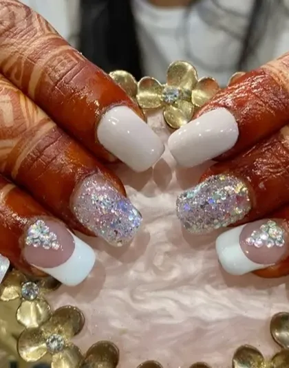 A beautiful bridal look on henna-adorned hands, featuring white tips, chunky iridescent glitter, and delicate crystal accents.