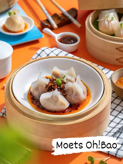 A vibrant shot of assorted dim sum in a bamboo steamer for Moets Oh! Bao, with a colorful orange background.