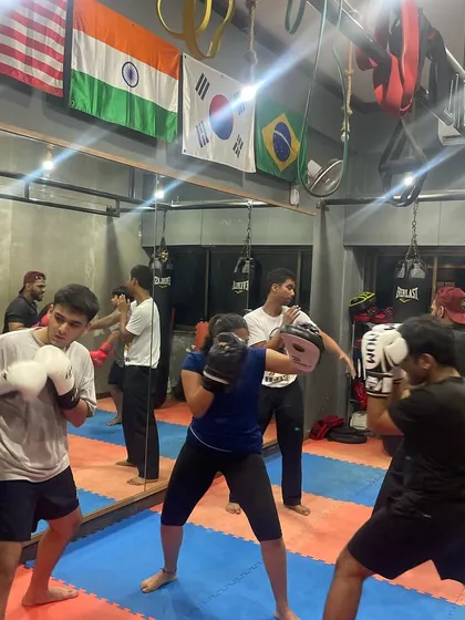 A snapshot of a busy kickboxing class where students partner up for pad work drills. The group dynamic provides motivation and a chance to practice with different partners.