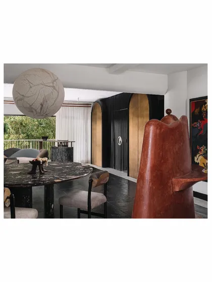 The living room of 'Aria' is a study in symmetry and drama. Two grand, arched cabinets frame the entrance to the media room, while a sculptural terracotta form and a dark marble dining table anchor the space with artistic and material richness.