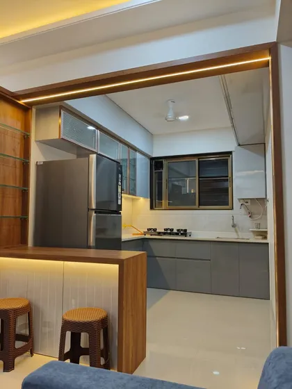 An example of an open-concept kitchen that flows into the living space. This setup includes a functional breakfast bar with integrated lighting, matte grey cabinets, and a dedicated space for a large refrigerator.