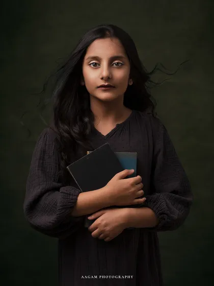 With her hair blowing gently, this young girl holds her books close. The portrait has a moody, cinematic feel, telling a story of a thoughtful and imaginative child.