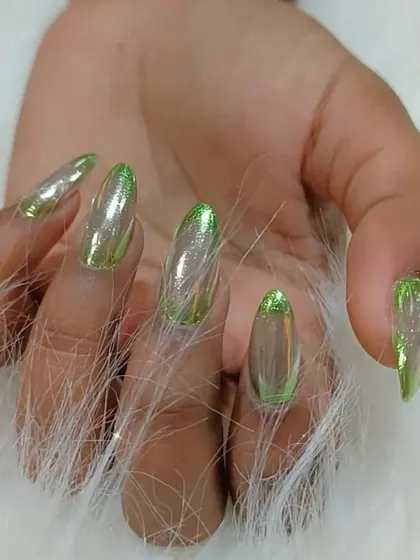 A unique set of long stiletto nails with a sheer base and a green chrome French tip for a modern, edgy look.