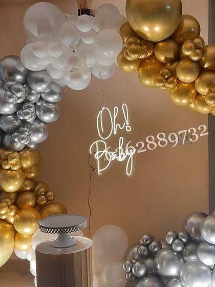 A chic and simple 'Oh Baby' shower decoration, using a ring backdrop with a garland of gold, silver, and white chrome balloons.