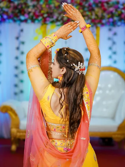 A beautiful back shot of the bride, showcasing her elegant hairstyle with floral details and her graceful dance pose. This highlights the intricate details of her Haldi look.