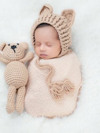 A sleeping newborn wearing a cute bear-eared hat, lying next to a matching teddy bear. A classic and heartwarming pose for any newborn session.