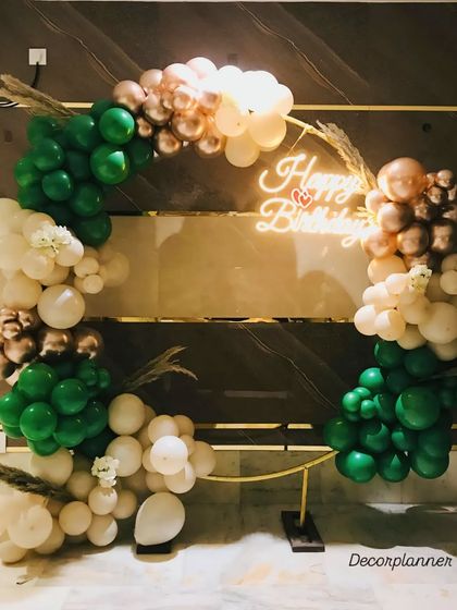 This elegant ring decor combines forest green, cream, and rose gold balloons for a sophisticated and earthy feel. The 'Happy Birthday' neon sign and dried pampas grass complete the modern, bohemian-inspired look.