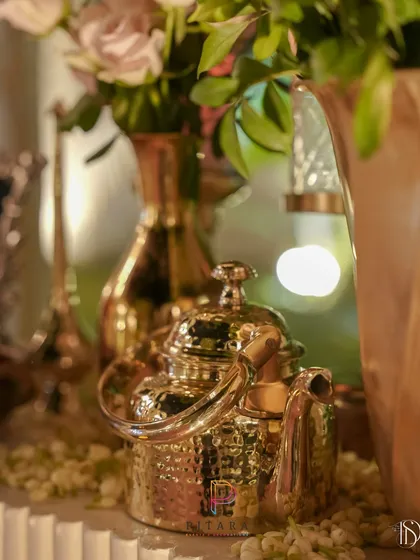 A hammered brass teapot shines in the candlelight, reflecting the warm glow of the event. We use metallic accents like this to add a touch of vintage luxury and shine.