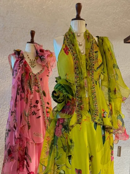 A splash of joy. This display features two floral printed outfits with ruffles and flowing layers in bright pink and lime green, perfect for a destination wedding.