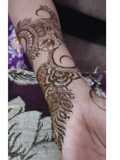 A close-up of a peacock and floral design on the wrist. The details in the feathers and petals are what make this piece special.