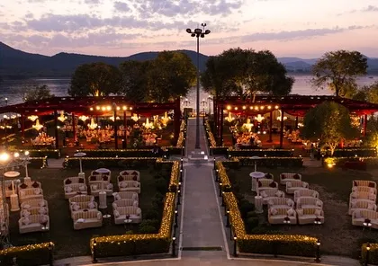 An evening view of a grand wedding setup by the lake in Udaipur. The warm lighting and symmetrical layout create a sense of order and opulence as dusk settles.