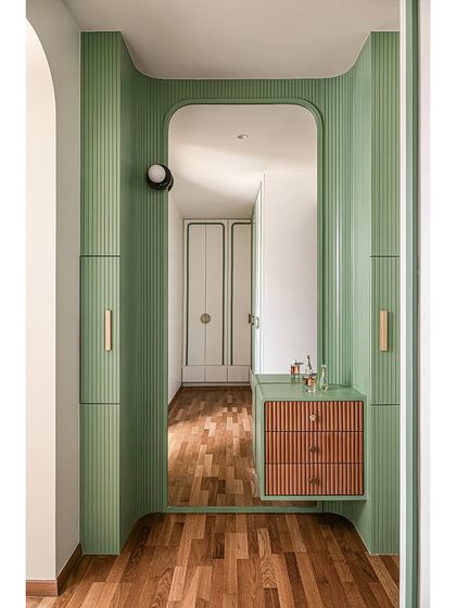 This unique entryway to the bedroom features curved, fluted walls in a vibrant green, with a built-in mirror and a floating vanity. It creates a fun and dramatic sense of arrival.