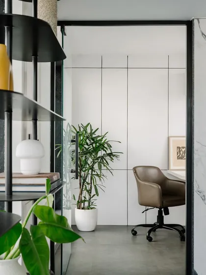 The reception area uses clean white wall panels and a sleek metal shelving unit to create a professional and welcoming first impression. The design provides a clear view into the adjacent meeting room.