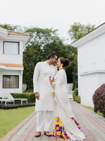 An intimate portrait of a couple in matching white outfits, about to share a kiss in a beautiful garden path, showcasing a quiet moment of love.