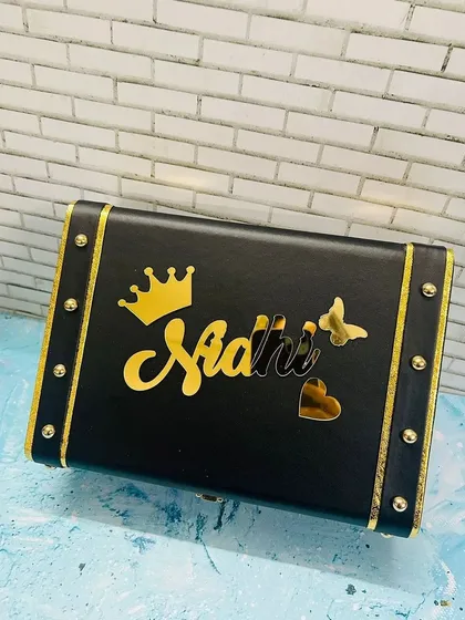Keep your treasures safe in this personalized keepsake trunk. Made from black leatherette with gold accents, it can be customized with a name and charms like the crown and butterfly shown here, making it a stylish storage solution.