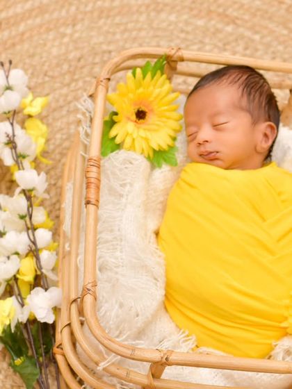 This little "son-shine" is sleeping peacefully in a basket, surrounded by yellow and white flowers. This setup demonstrates a bright and cheerful theme perfect for celebrating a new arrival.