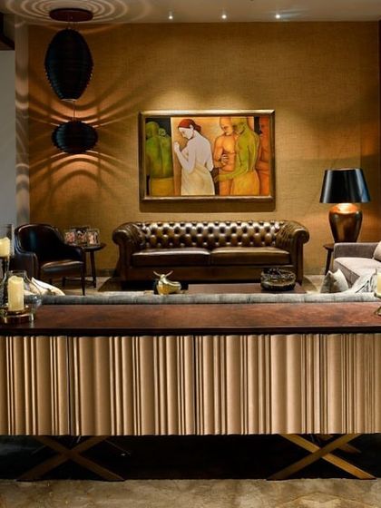 A view across the living room, showing a custom console table with a fluted brass-finish base. The space is layered with warm lighting, rich textures, and carefully curated art.