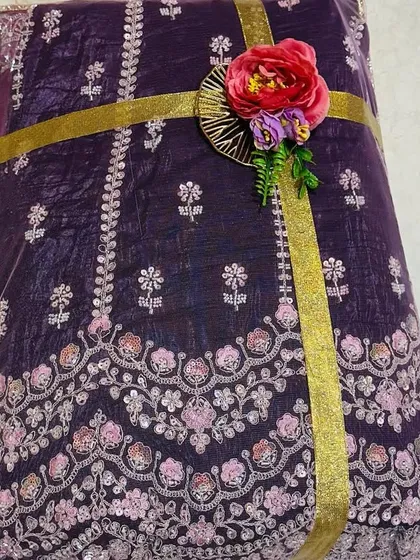 The details make all the difference. This close-up shows a richly embroidered purple fabric, perfect for a bridal lehenga, secured with a simple gold ribbon and a delicate floral accent to complement its intricate design.