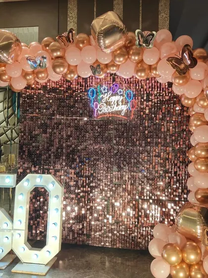 The full setup for a 50th birthday, featuring a rose gold sequin wall, a balloon arch with butterfly accents, and a large light-up marquee number.