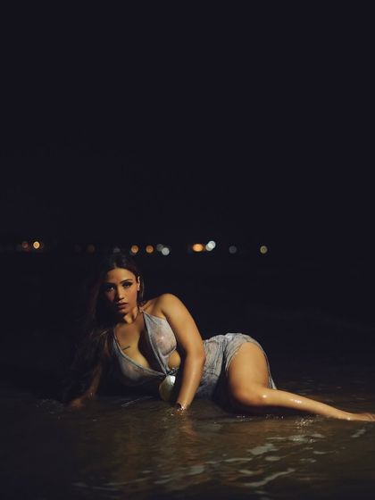 A wide shot that captures the solitude and drama of a night shoot on the beach. The composition emphasizes the model against the vast darkness of the sea and sky.
