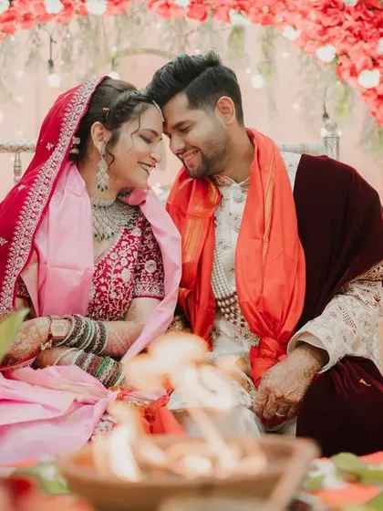 The couple shares a quiet moment together during their wedding ceremony, seated before the sacred fire under an arch of red flowers.