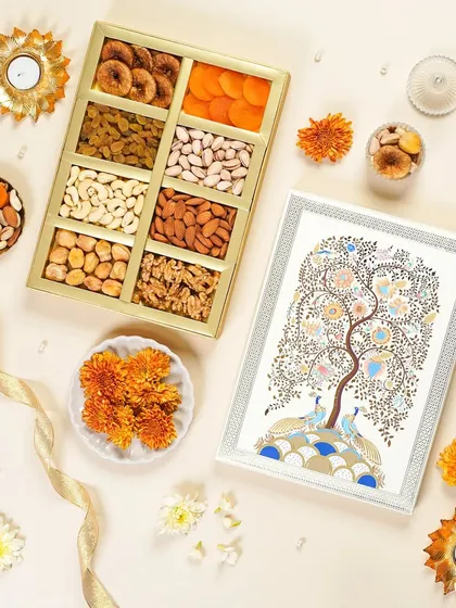 A top-down shot of an artistic dry fruit gift box featuring a peacock tree design. The composition with fresh flowers and diyas creates a serene and culturally rich image for festive promotions.
