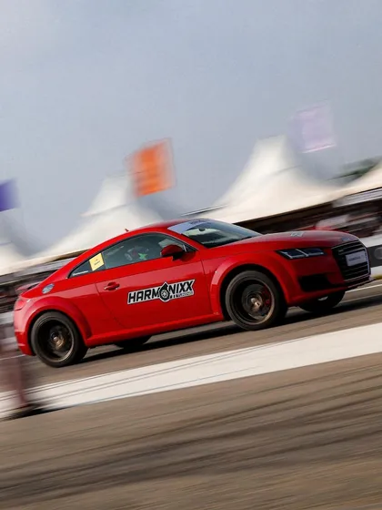 A red Audi TT coupe with Harmonixx branding speeds past the spectator tents. This shows how brands get visibility right alongside the on-track action.