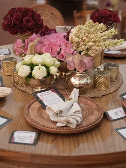 An elegant table setting with a mix of roses and tuberoses, wooden plates, and custom menu cards. Every detail is thoughtfully curated to match the event's theme.
