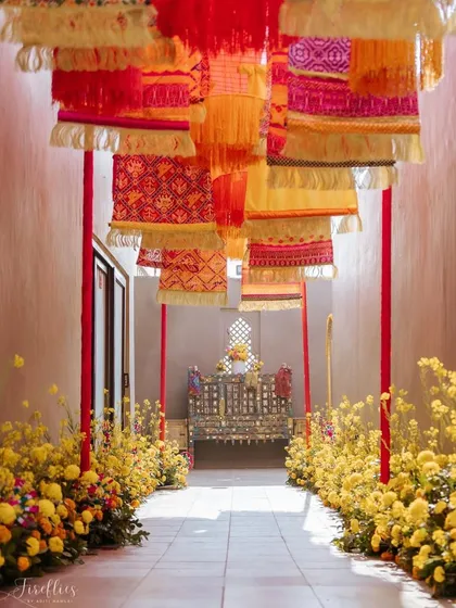 An entryway decorated with hanging Rajasthani 'bandhani' and 'leheriya' fabric panels. This colorful passage, lined with marigold flowers, led guests to a beautifully decorated seating area.