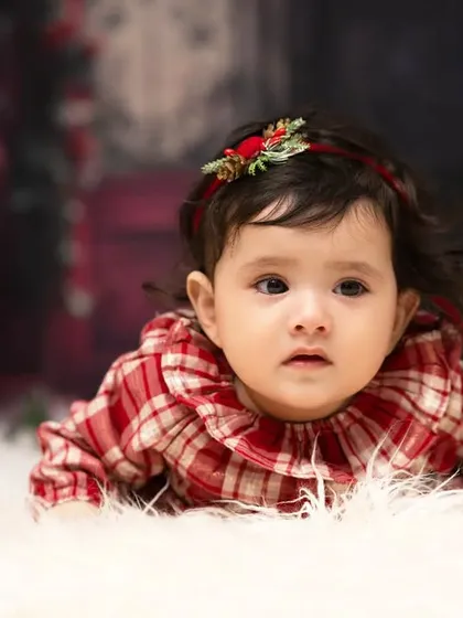 A thoughtful gaze from a sweet baby girl. Dressed in a festive plaid top, her curious expression is the focus of this simple and beautiful portrait.