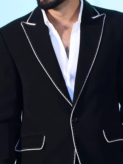 A close-up of the chest and lapel of the piped black suit. The open-collar styling gives a modern, relaxed feel to this formal look.
