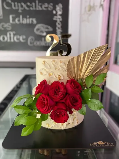 A sophisticated cake for a 25th celebration, featuring a cascade of fresh red roses and a modern, gold palm spear accent.
