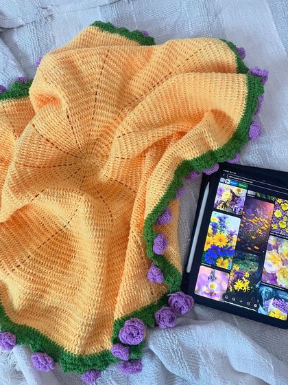 The bouquet blanket fully opened, revealing its circular shape and the beautiful purple rose border. It's a cozy and unique piece of functional art.