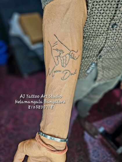 This line art tattoo shows a parent's hand holding a child's, with "Mom Dad" written below. It's a simple yet powerful design symbolizing family bonds.