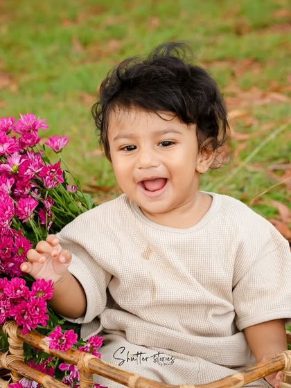 A big, happy smile from the baby boy in the basket, clearly enjoying his outdoor photoshoot.