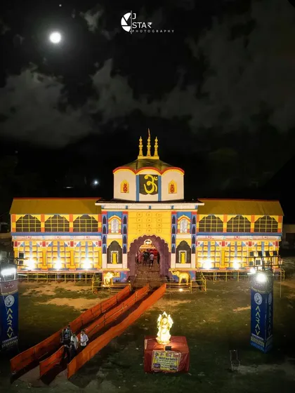 A ground-level perspective of a colorful pandal entrance, designed to look like a grand temple. Even without a drone, I focus on creating a powerful image that captures the structure's beauty under the full moon.