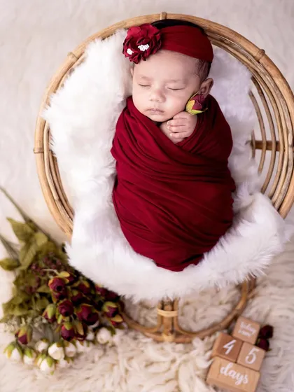 This newborn is wrapped snugly in a rich red swaddle, resting in a rustic cane basket. The color contrast and textures make for a visually striking portrait.