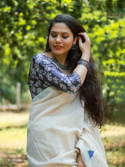 An elegant outdoor portrait in a classic white and blue saree. The lush green background makes the subject stand out beautifully.