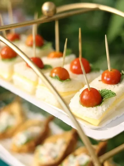 A close-up of our delicate mini sandwiches, topped with a cherry tomato and fresh basil leaf. A simple, fresh, and elegant bite for your guests.