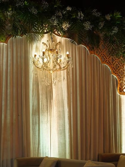 A close-up of the backdrop for the seating deck, featuring a beautiful chandelier against softly lit drapes and a jali arch.