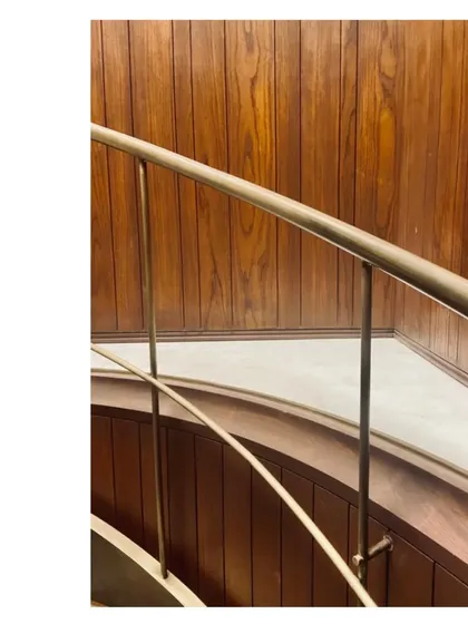 An aged brass handrail meets a curved, wood-paneled wall. We love the small details, the points where different materials connect and the hand meets the architecture.